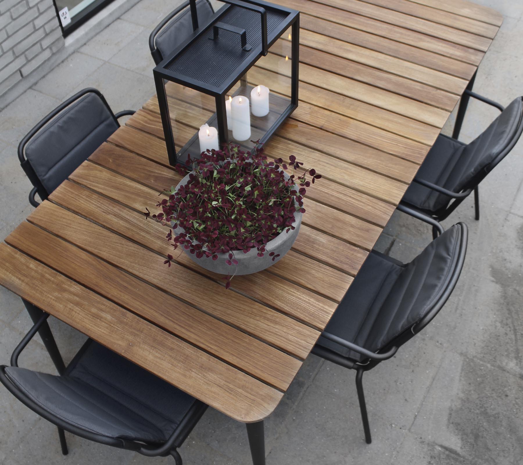 Une table en bois avec des chaises noires, présentant un grand pot de fleurs et un centre de lanterne à bougie.