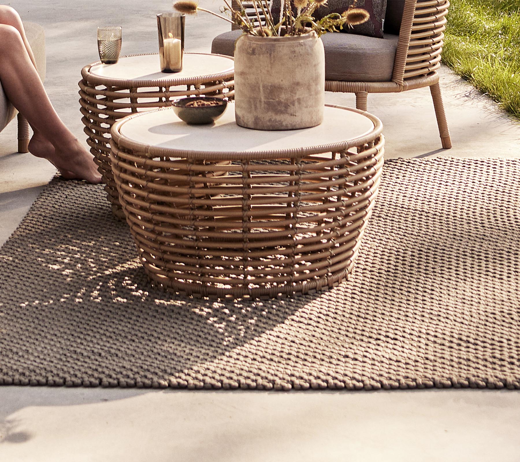 Un coin salon confortable avec des tables tissées, un vase décoratif et un tapis texturé, parfait pour rehausser un espace élégant.