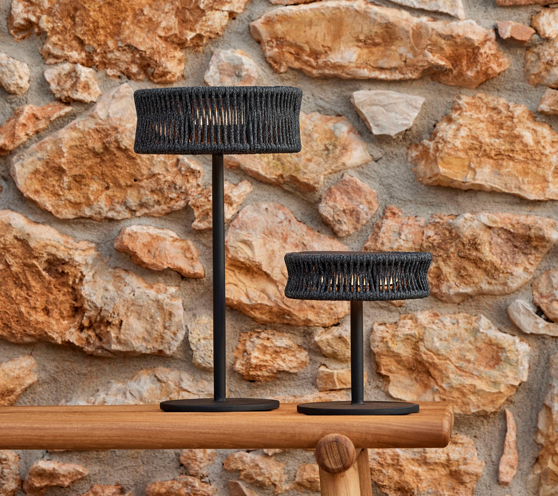 Deux lampes de table élégantes avec un design tressé, se détachant sur un mur en pierre texturé, créant une atmosphère élégante et accueillante.