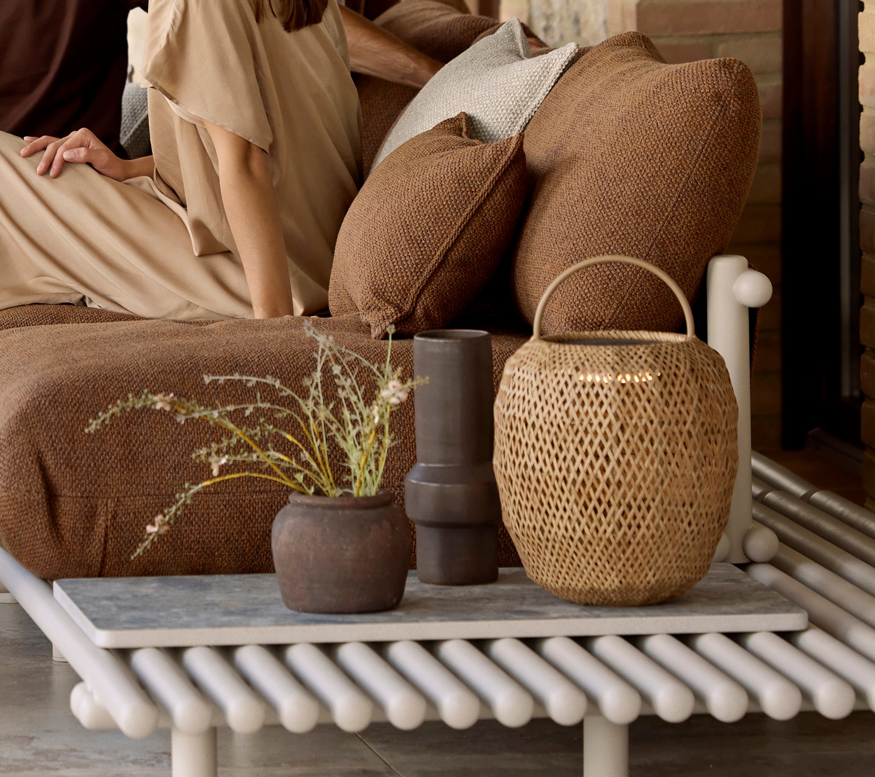 Un arrangement décoratif avec une lampe à incandescence, des coussins texturés et divers vases sur une table unique à lattes.