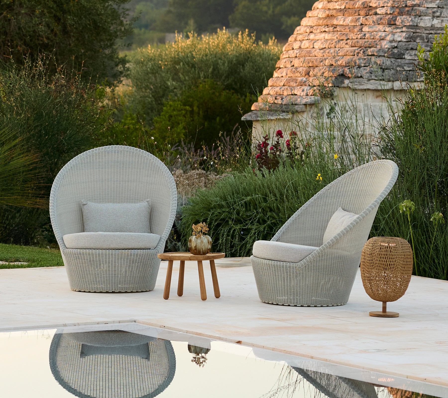 Deux fauteuils gris et une table d'appoint en bois à côté d'une piscine dans un cadre extérieur moderne.