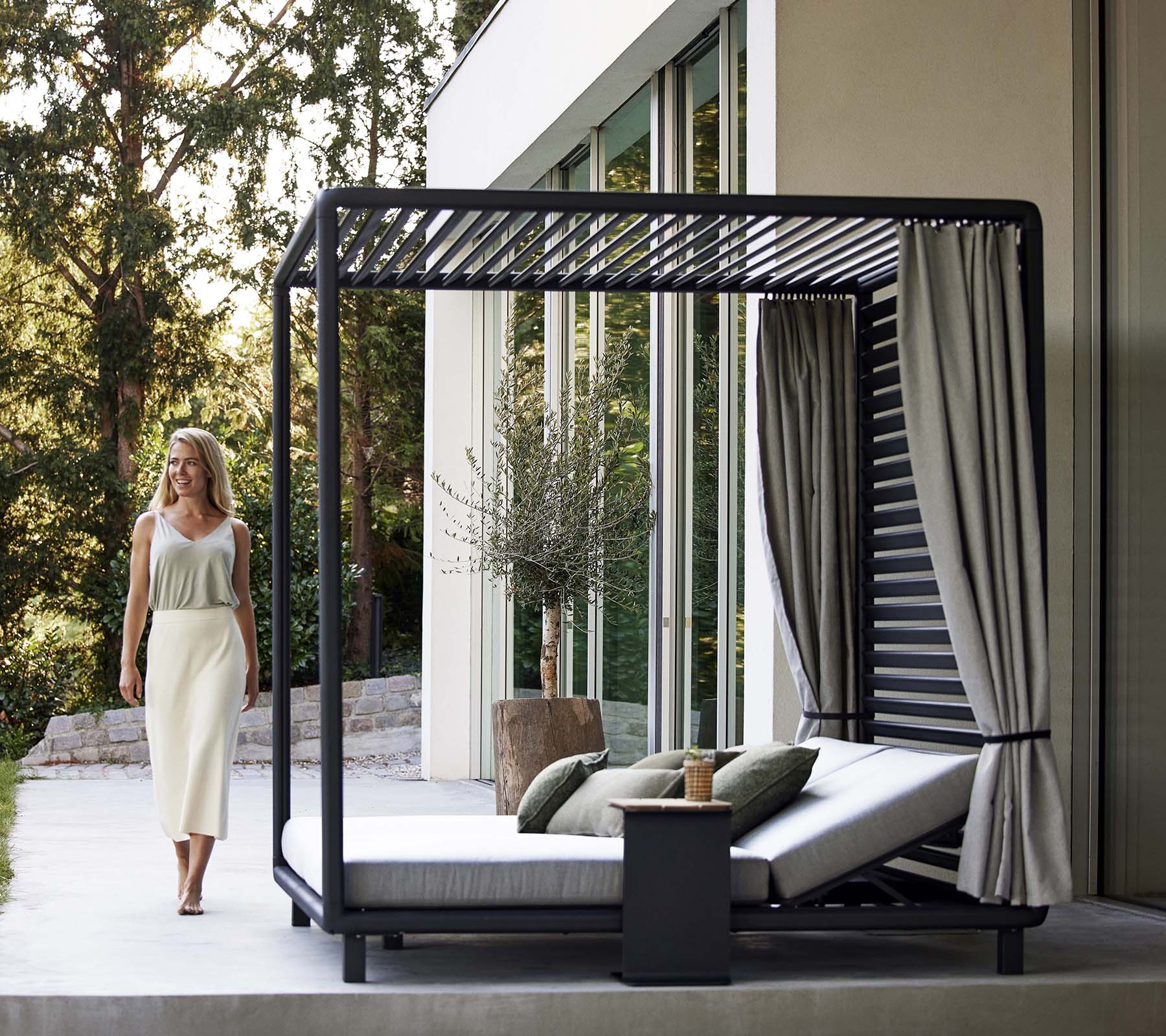 Une cabine élégante avec un design épuré, des coussins doux, des rideaux et une petite table d'appoint, située dans un environnement naturel serein.