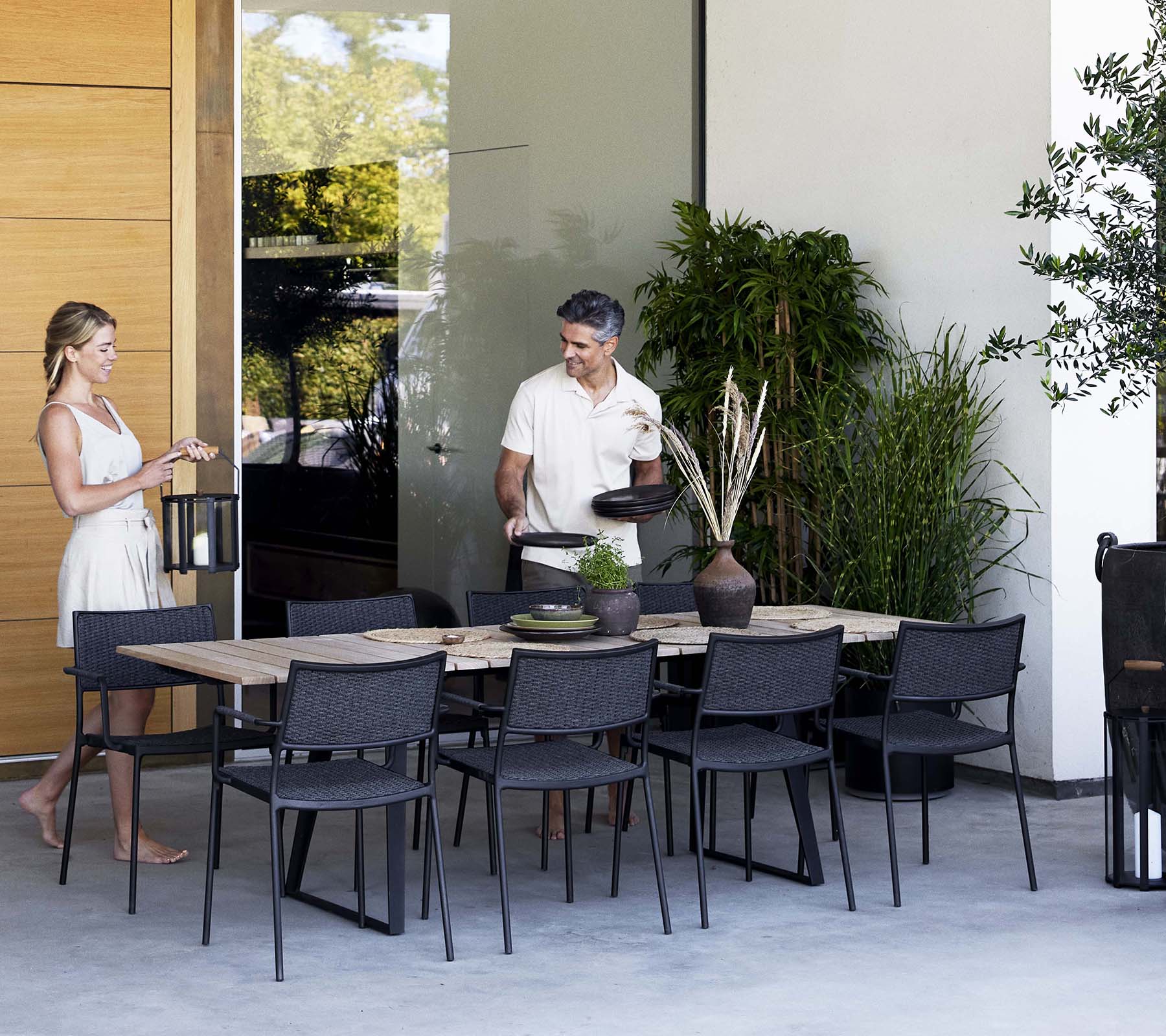 Une femme et un homme engagent une conversation près d'une table à manger élégante entourée de chaises modernes et de verdure.