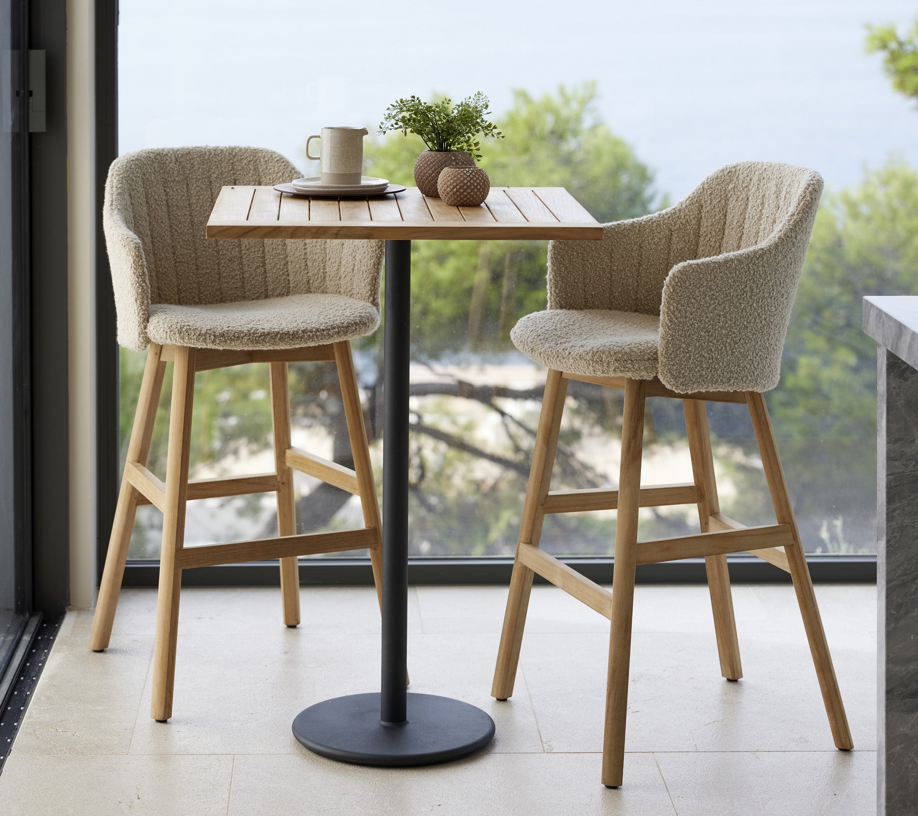 Une petite table avec deux chaises rembourrées, une tasse et des éléments décoratifs, placés contre un fond naturel.