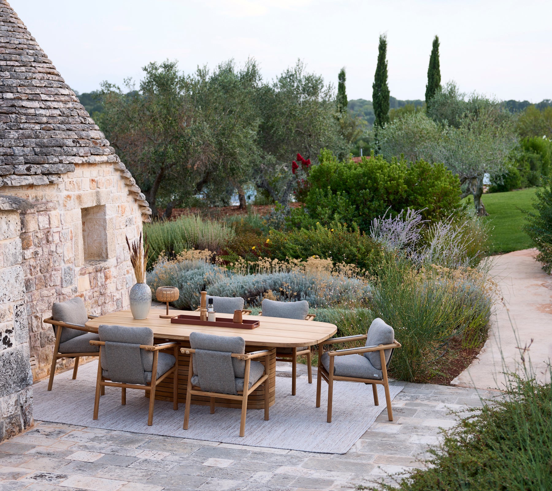Installation moderne de repas en plein air avec une table ronde et des chaises grises entourées de verdure.