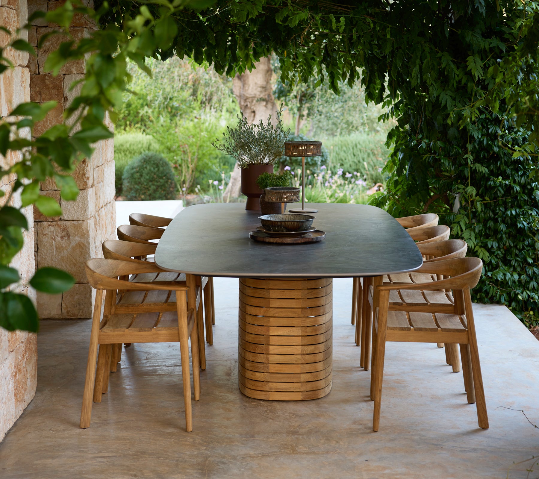 Table à manger d'extérieur moderne avec des chaises en bois entourées de verdure.