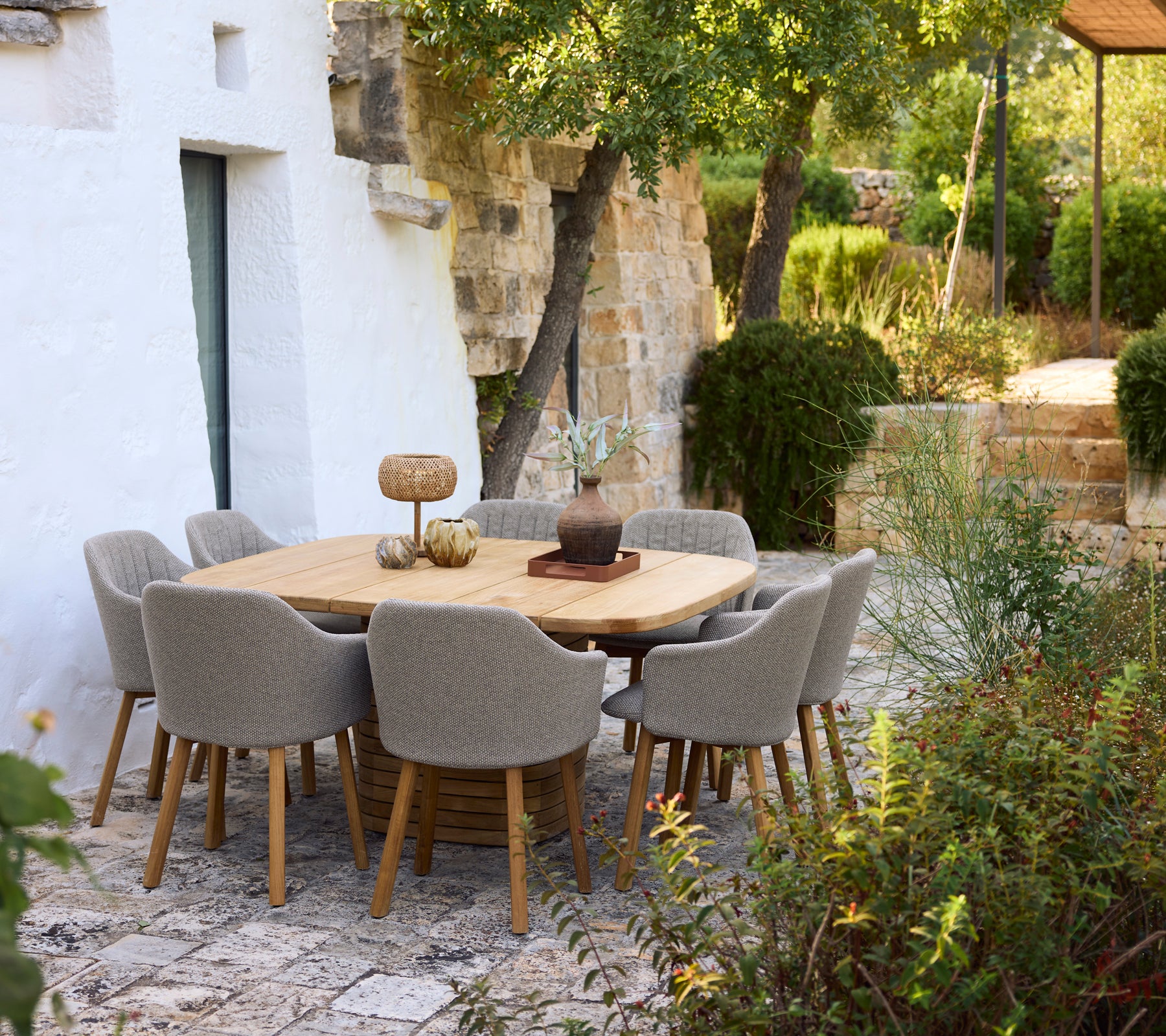 Table à manger en bois moderne entourée de chaises grises dans un cadre de jardin.