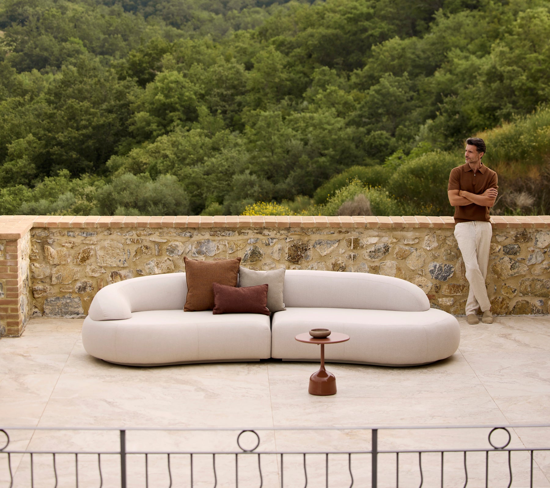 Canapé lounge Mellow avec des coussins Rise et une table basse Glaze, placés devant un arrière-plan verdoyant.