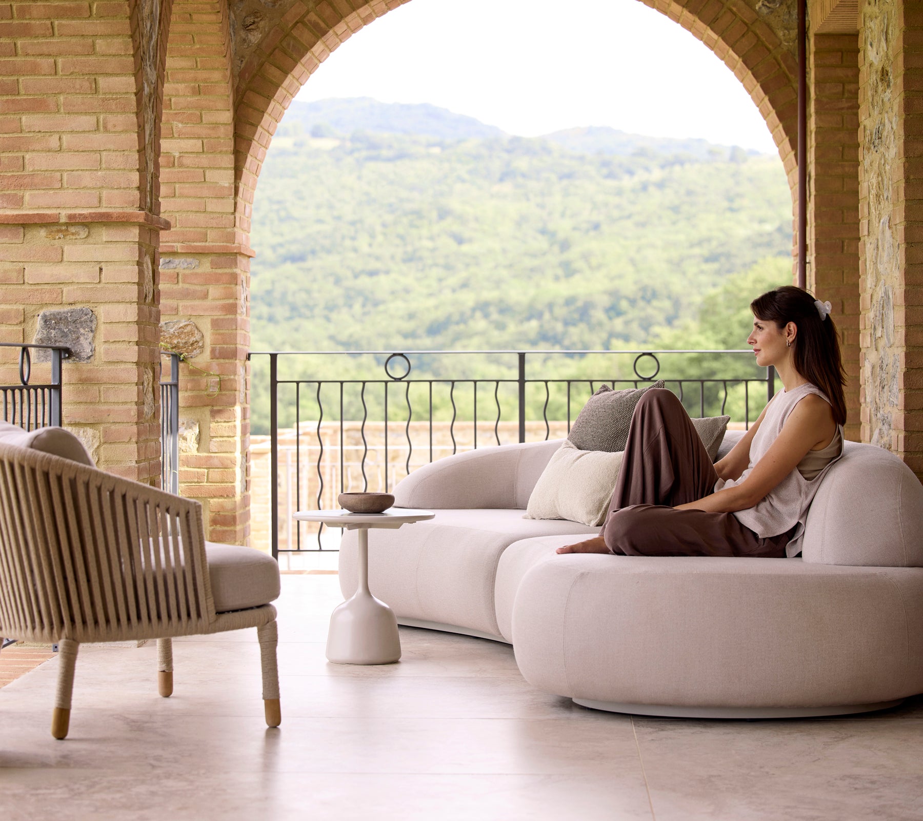 Un coin salon serein avec un canapé lounge doux, une chaise lounge Moments et une table basse Glaze, avec une végétation luxuriante en arrière-plan.