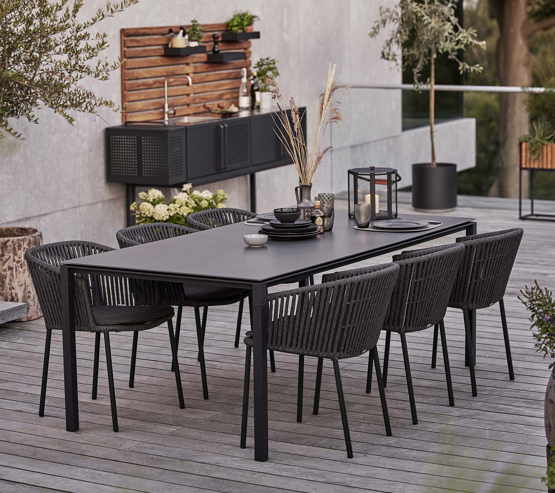 Une table noire élégante équipée de six chaises Moments, avec de la vaisselle et des éléments décoratifs pour une expérience de dîner accueillante.