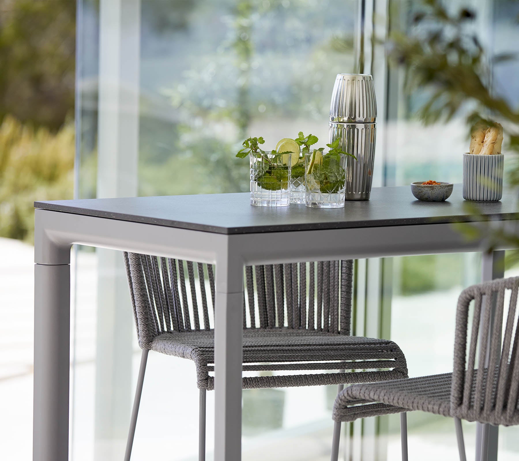 Une table moderne avec deux chaises élégantes, ornée de plantes décoratives et d'un petit plat, située dans un décor lumineux et ouvert.