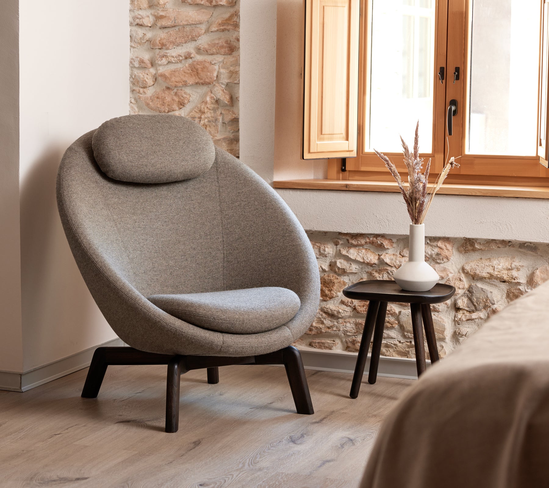 Chaise rembourrée élégante et incurvée avec un appui-tête confortable, accompagnée d'une petite table d'appoint avec un vase et des éléments décoratifs.