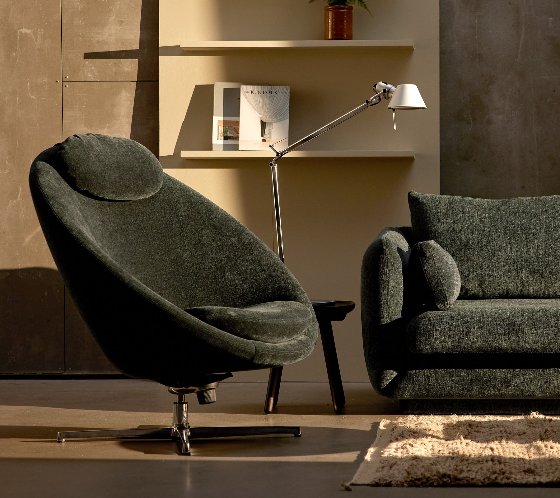 Fauteuil Pace en chenille vert foncé à côté d'un canapé Bloom, complété par une lampe élégante et une décoration d'étagère minimaliste.
