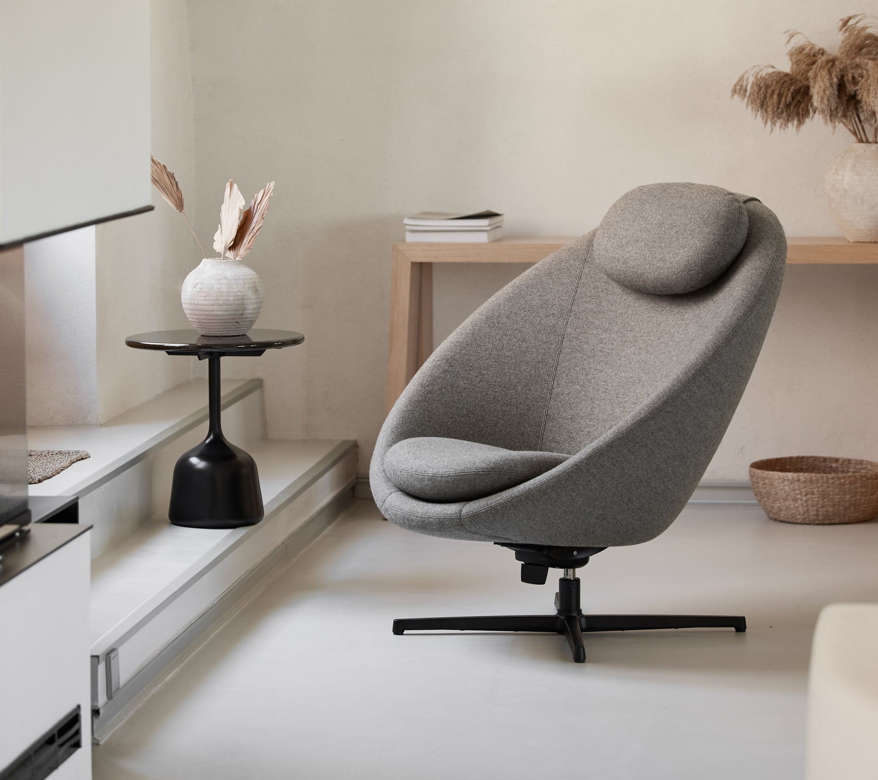 Chaise grise élégante avec une forme courbée et un appui-tête confortable, complétée par une table d'appoint minimaliste et des éléments décoratifs.