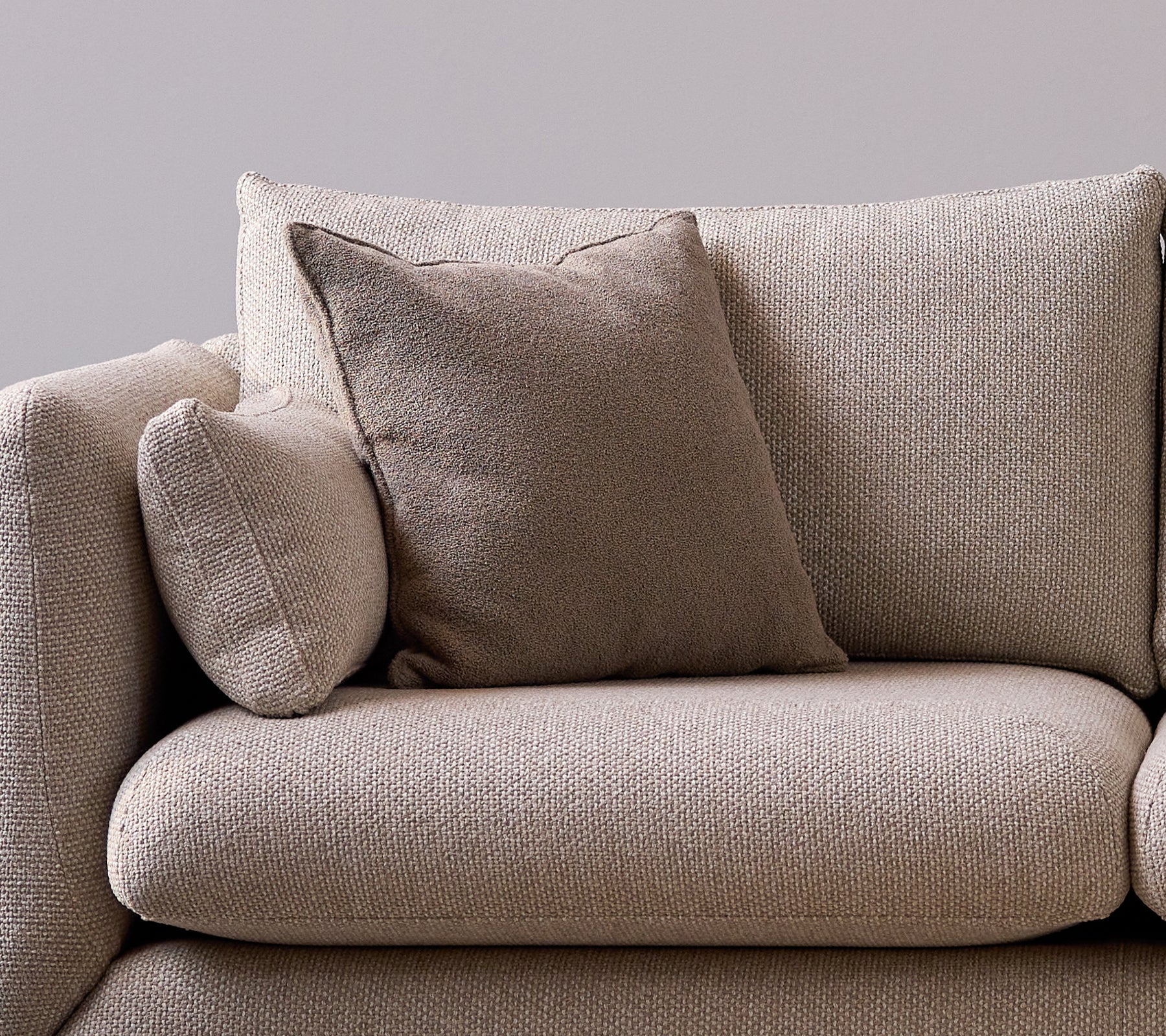 Coussin parfumé taupe sur un canapé doux et texturé, ajoutant une touche cosy et élégante à l'espace salon.