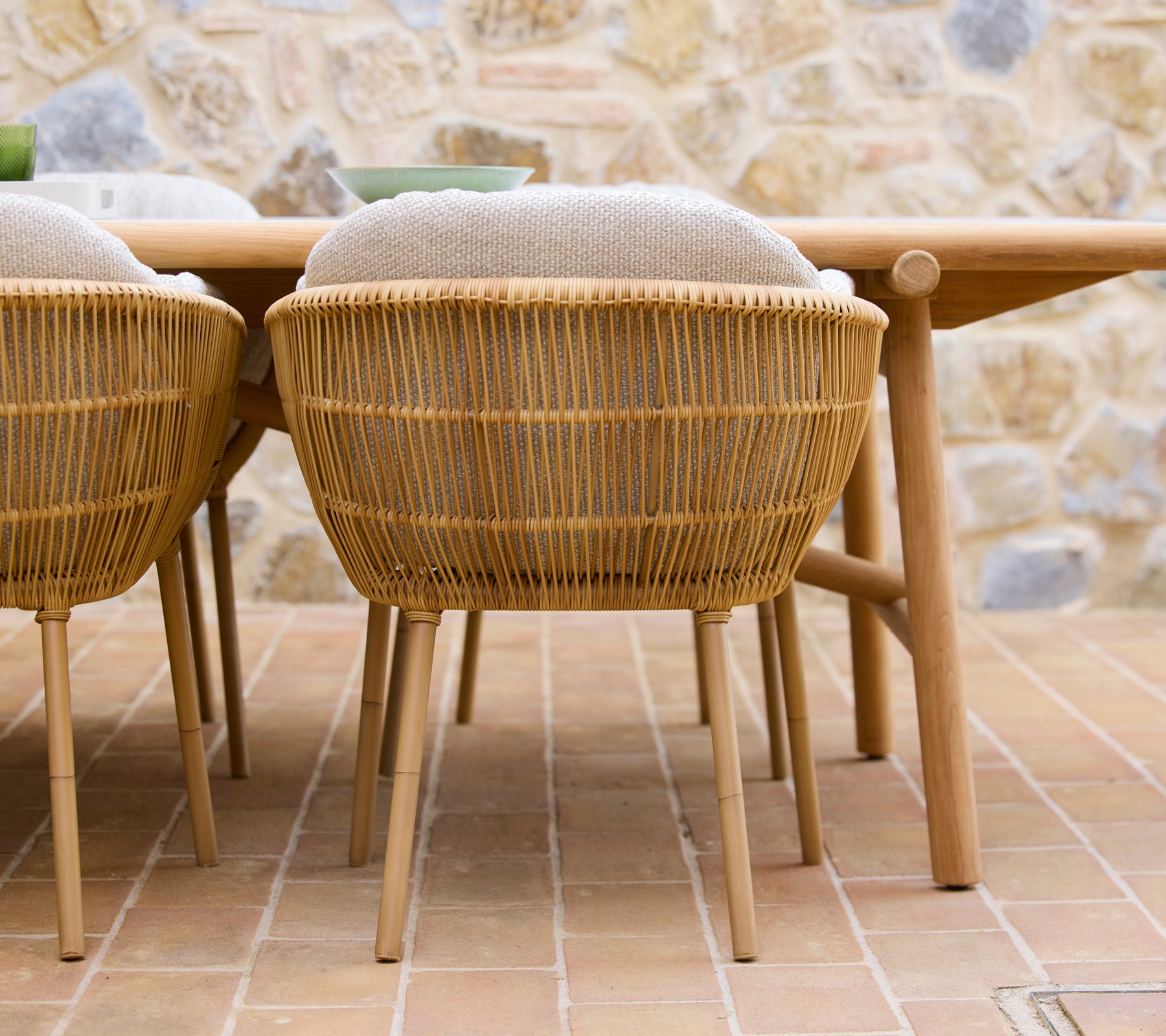 Deux chaises de salle à manger tissées avec des pieds en aluminium positionnées à côté d'une table à manger en bois, ayant une esthétique naturelle.