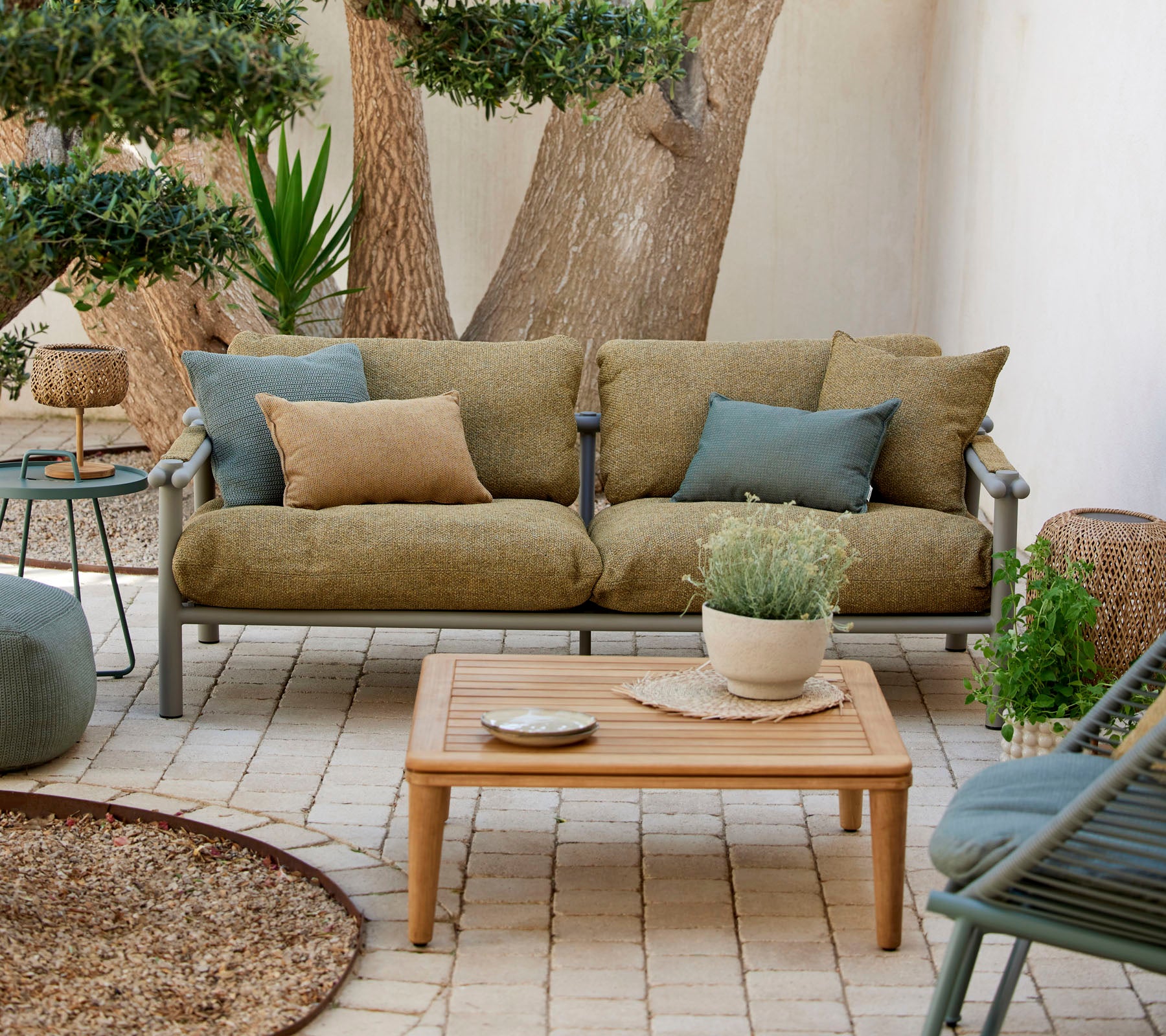 Espace de détente confortable avec un canapé vert avec des coussins, une table basse en bois et des plantes décoratives dans un cadre serein.