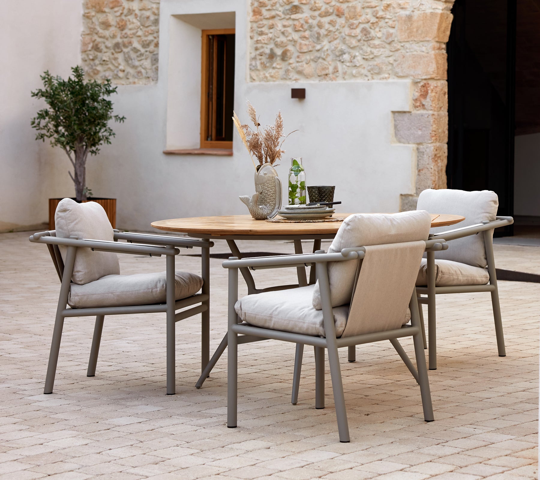 Table à manger moderne avec un plateau en bois et des cadres en aluminium, accompagnée de chaises douces et rembourrées, sur fond texturé.