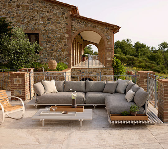 Agencement de sièges confortable avec un canapé gris et une table basse moderne avec un pot de fleurs, sur fond de paysage pittoresque.