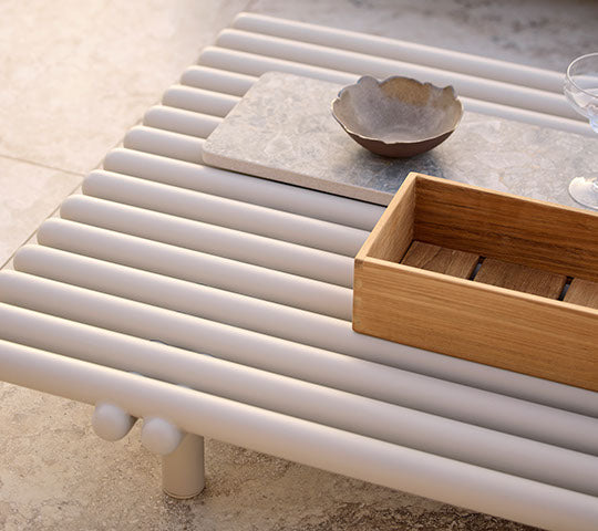 Table basse en aluminium avec design à lamelles, comprenant une boîte de rangement en bois et un bol en céramique sur une surface minimaliste.