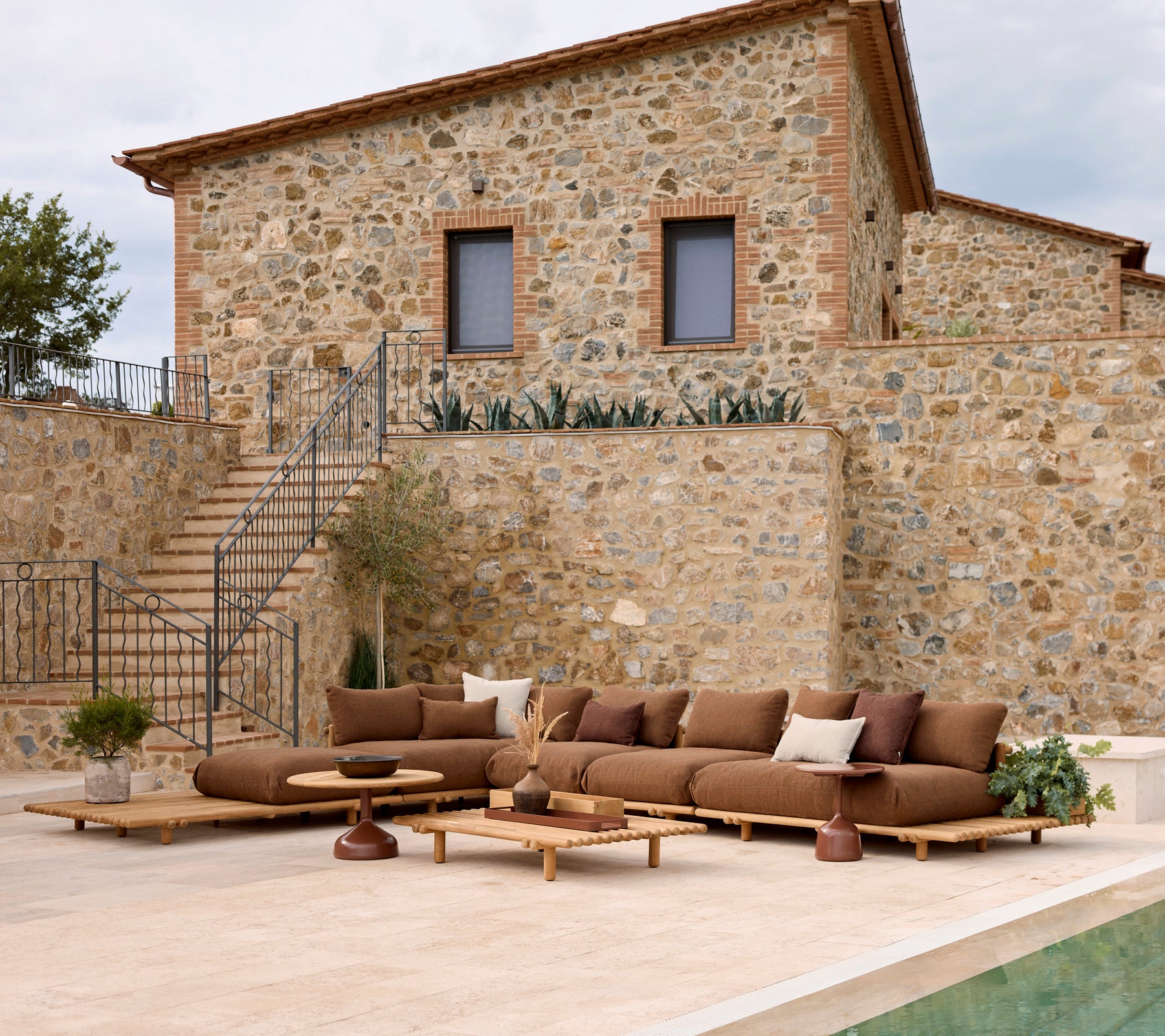Canapé de salon avec des coussins moelleux à côté d'une table basse élégante, contre un mur en pierre. Des jardinières ajoutent une touche naturelle.