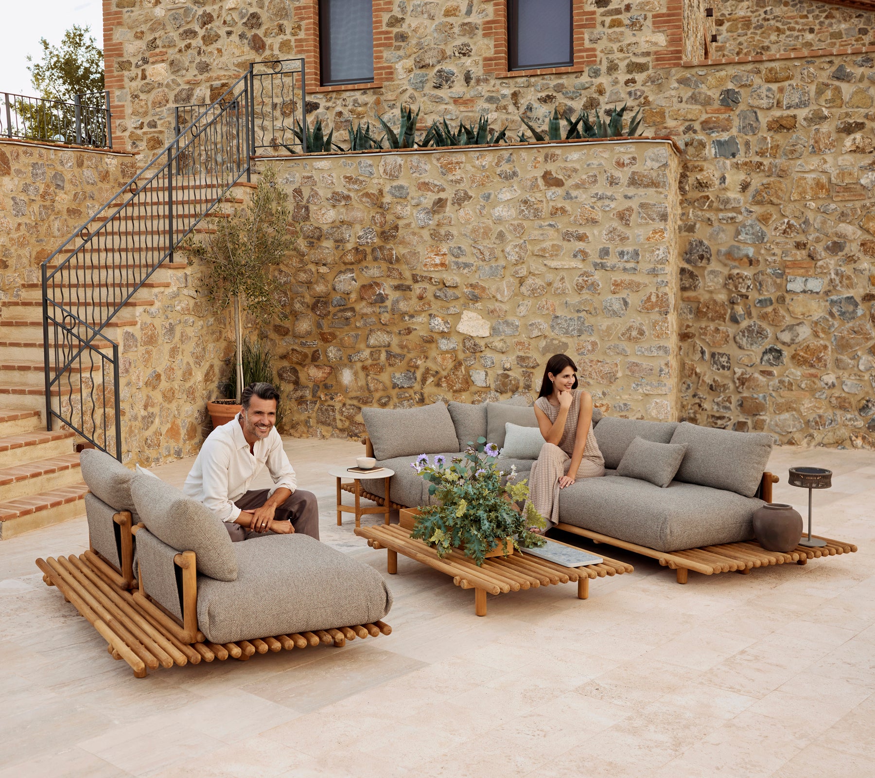Un espace salon élégant avec des meubles en teck, des coussins gris moelleux, accentué par de la verdure et une table basse moderne.