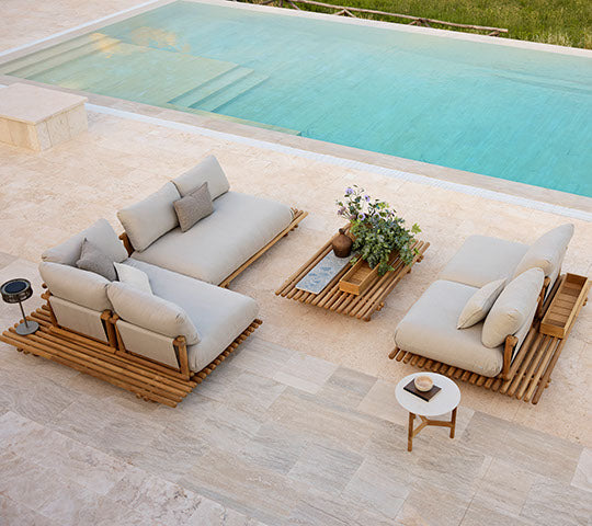 Mobilier en teck élégant avec des coussins Natte, complété par une table basse assortie et une plante en pot, placée à côté d'une piscine tranquille.