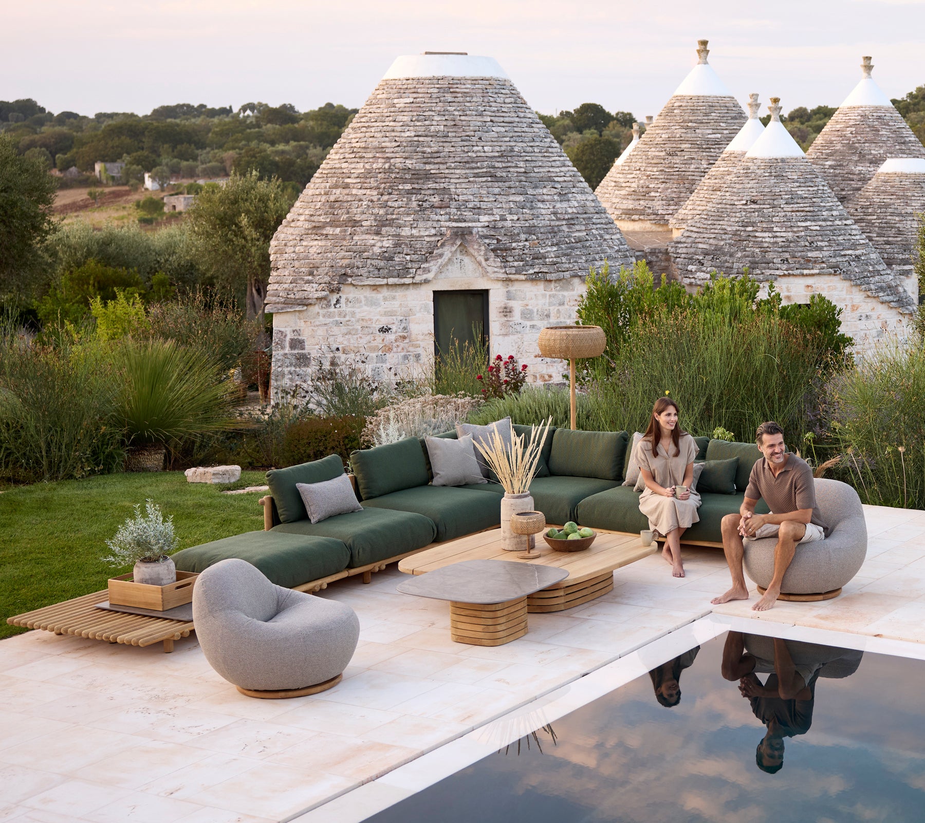 Espace lounge moderne en extérieur avec un canapé vert, une chaise grise et une table basse ronde.