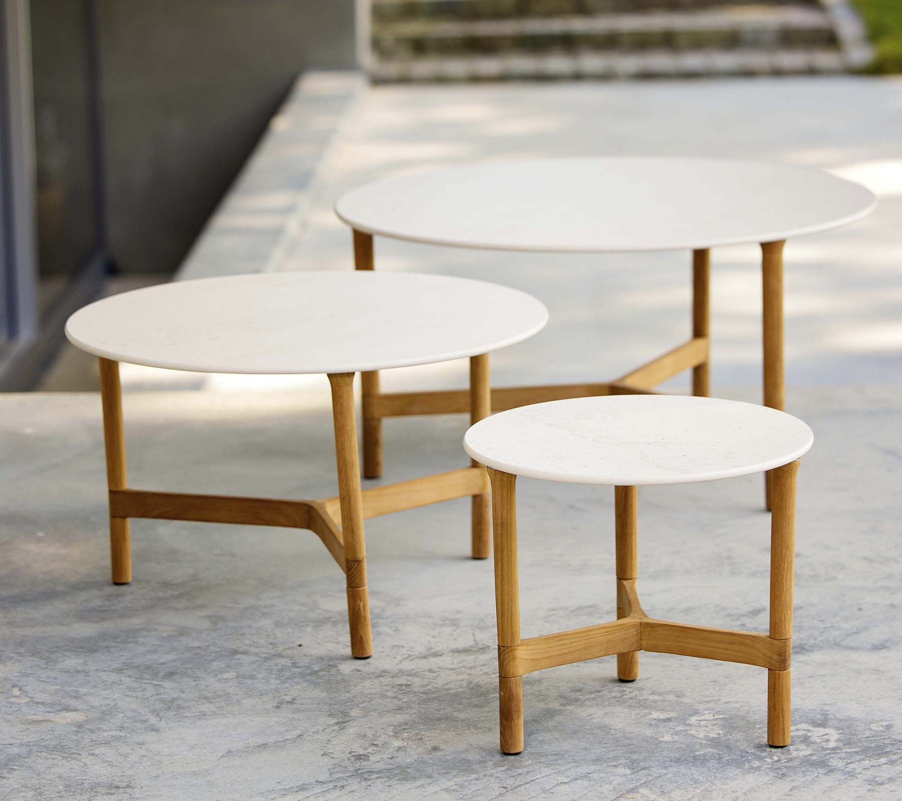 Trois tables basses modernes de différentes tailles avec des plateaux blancs et des pieds en bois, affichant un design élégant et minimaliste.