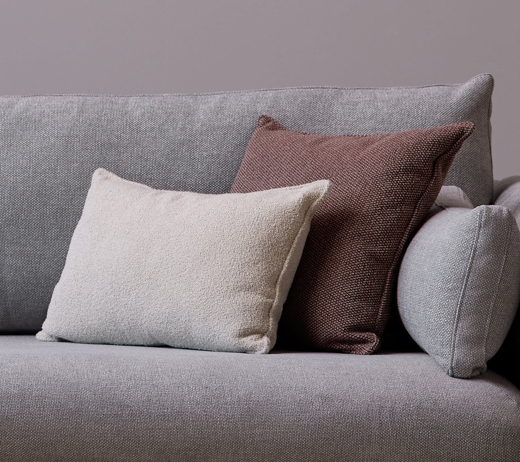 Un coussin d'appoint Scent blanc et un coussin Wove bordeaux foncé sont placés sur un canapé gris.