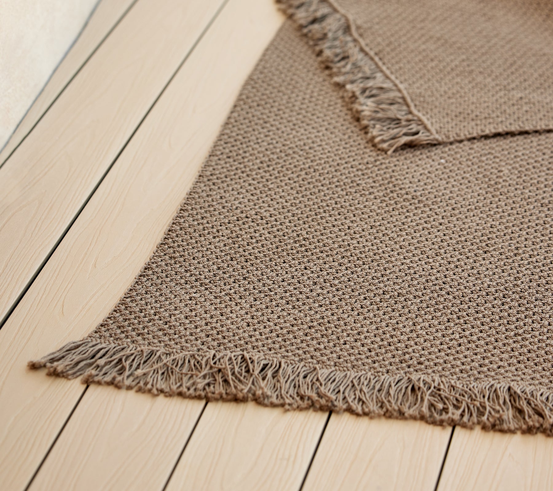 Un tapis en tricot texturé avec des bords à frange, présentant une couleur chaude et neutre, améliorant son esthétique cosy.