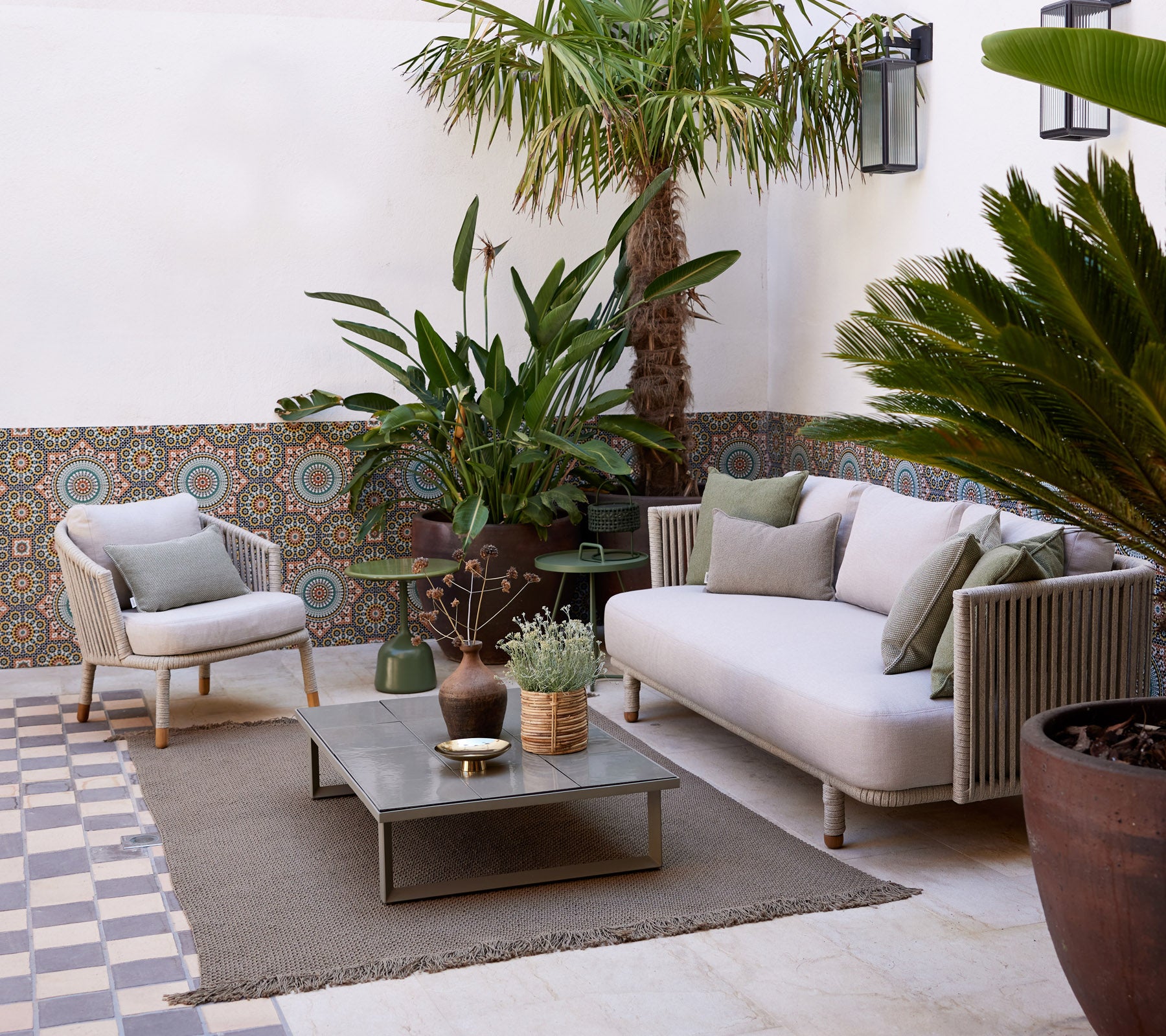 Espace salon confortable avec un canapé clair, des plantes en pot, une table décorative et un sol texturé, créant une ambiance sereine.