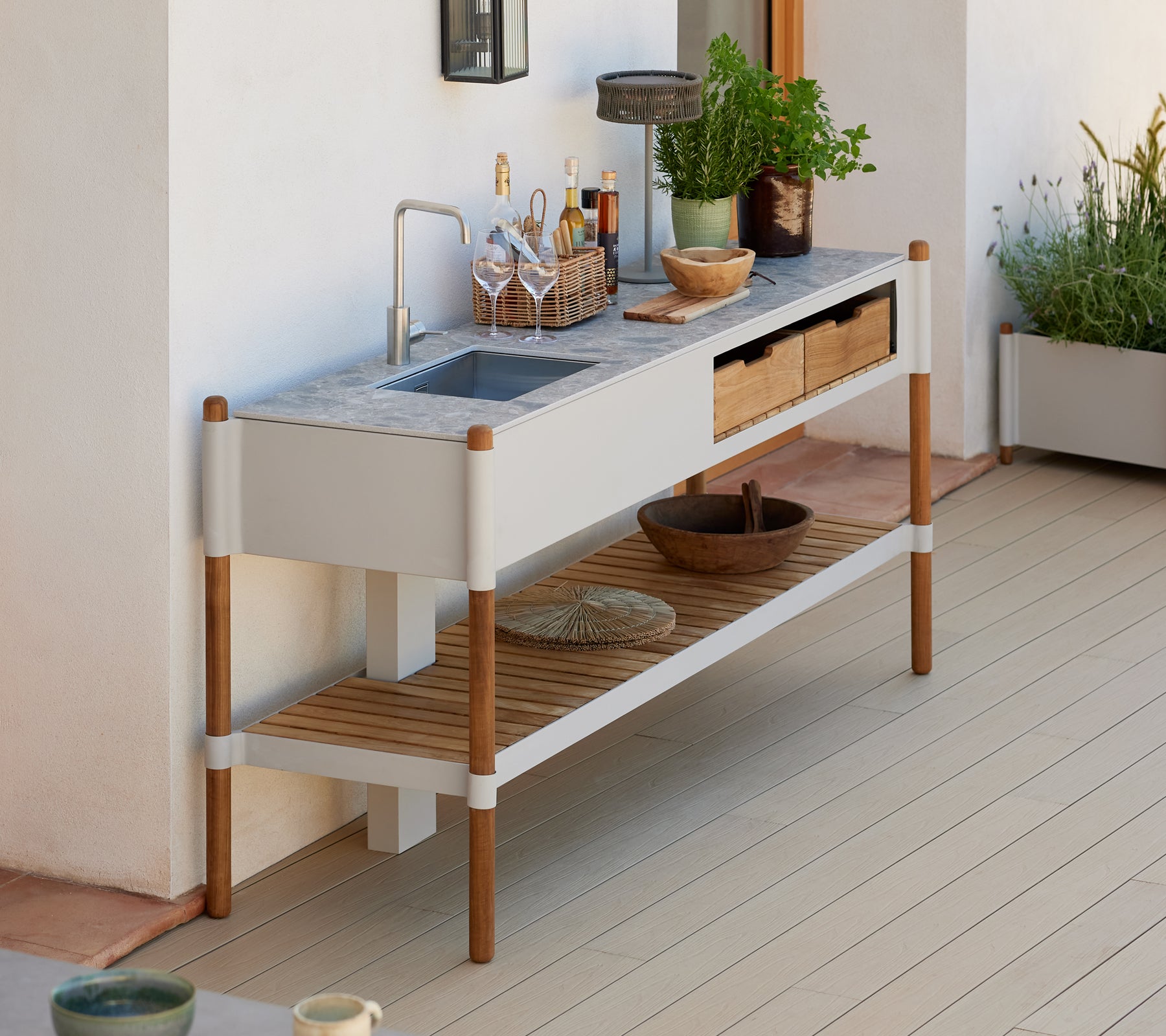 Un évier de jardin moderne et minimaliste avec un plan de travail en granit, des tiroirs de rangement en bois et des arrangements de plantes décoratives.