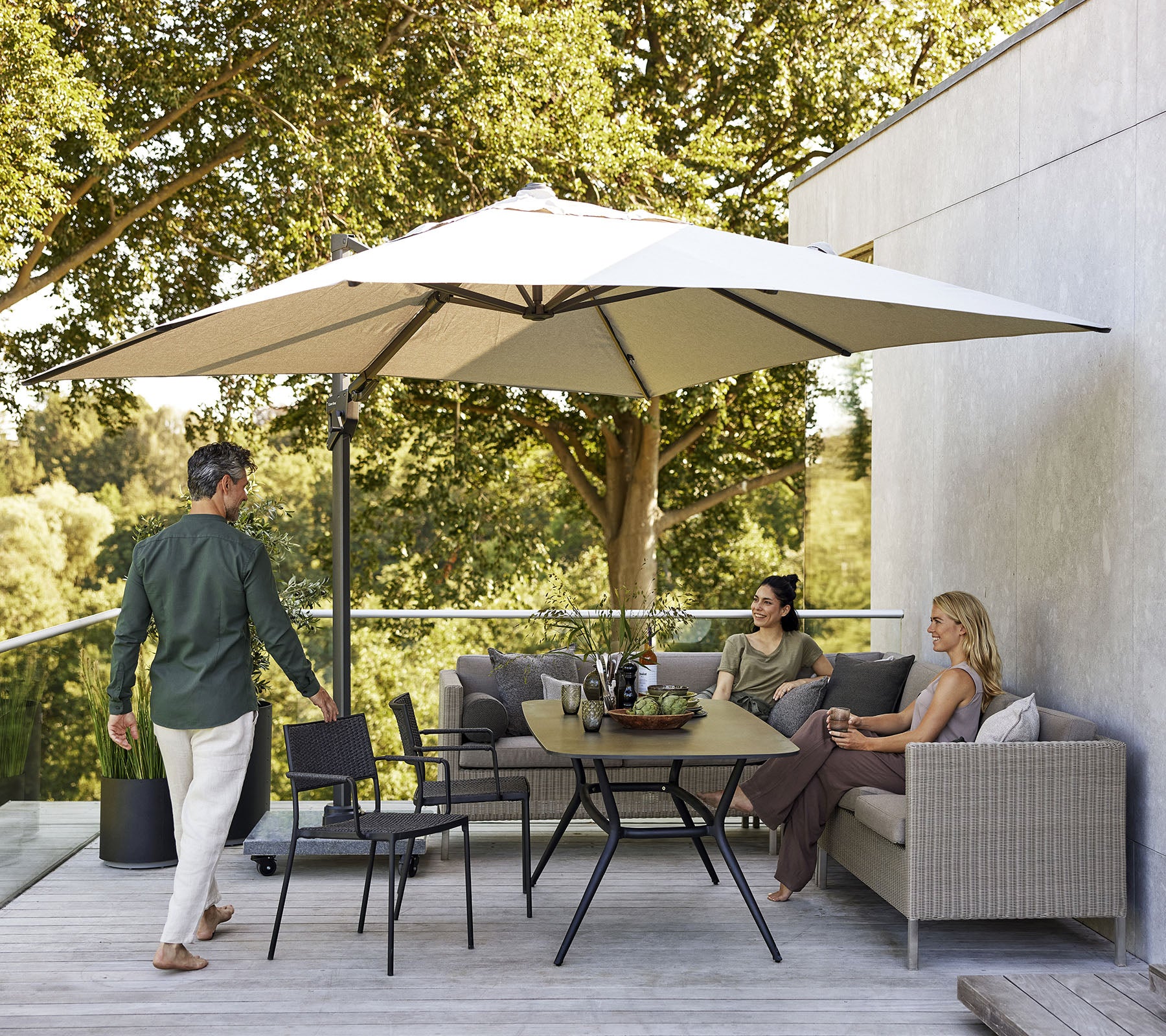 Un espace de sièges élégant avec un grand parasol, comprenant un canapé, des chaises et une table à manger entourée de verdure luxuriante.